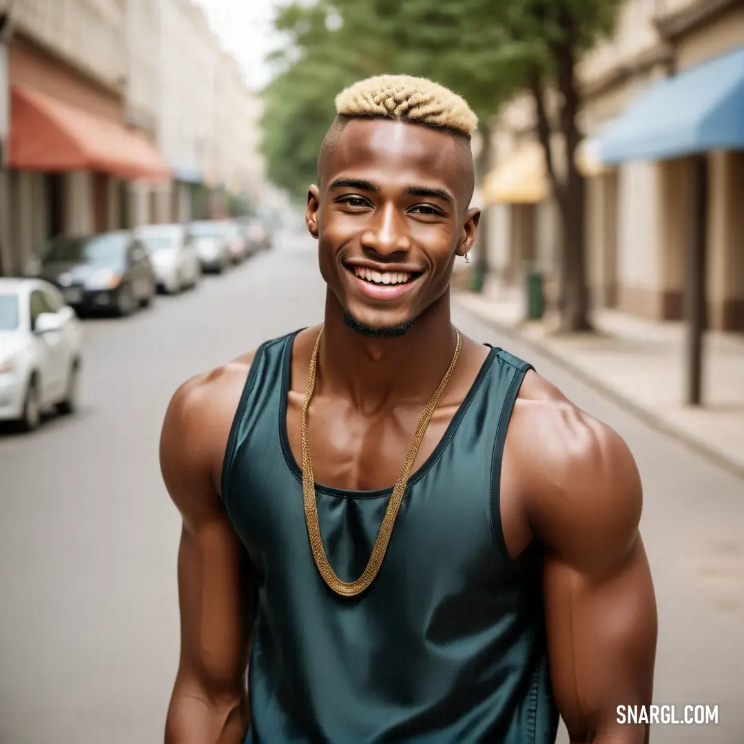 Man with a gold chain around his neck and a green shirt on a street with cars parked on the side of the road