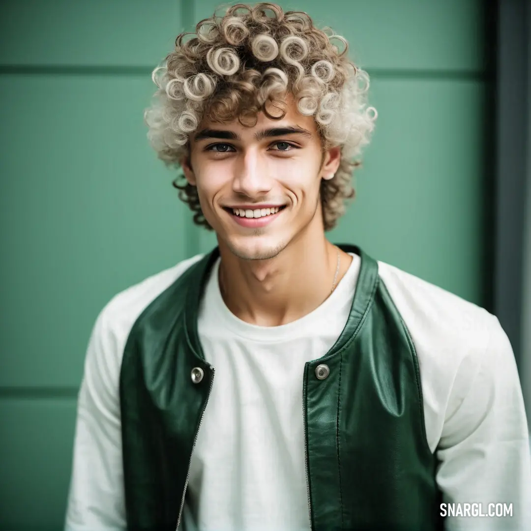 Man with curly hair and a green vest smiling at the camera