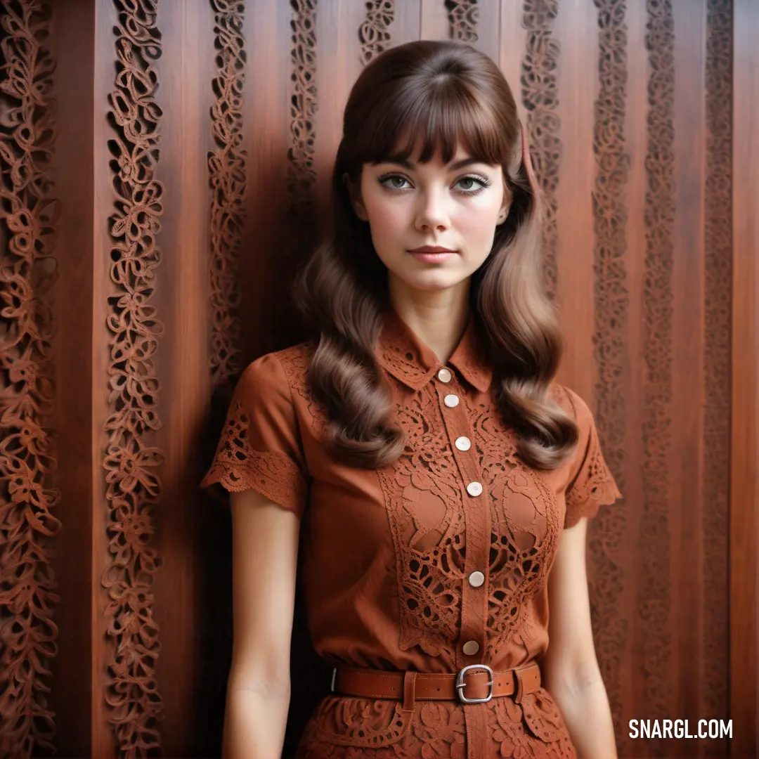 Woman standing next to a wooden wall wearing a brown dress and a belted shirt with a lace pattern