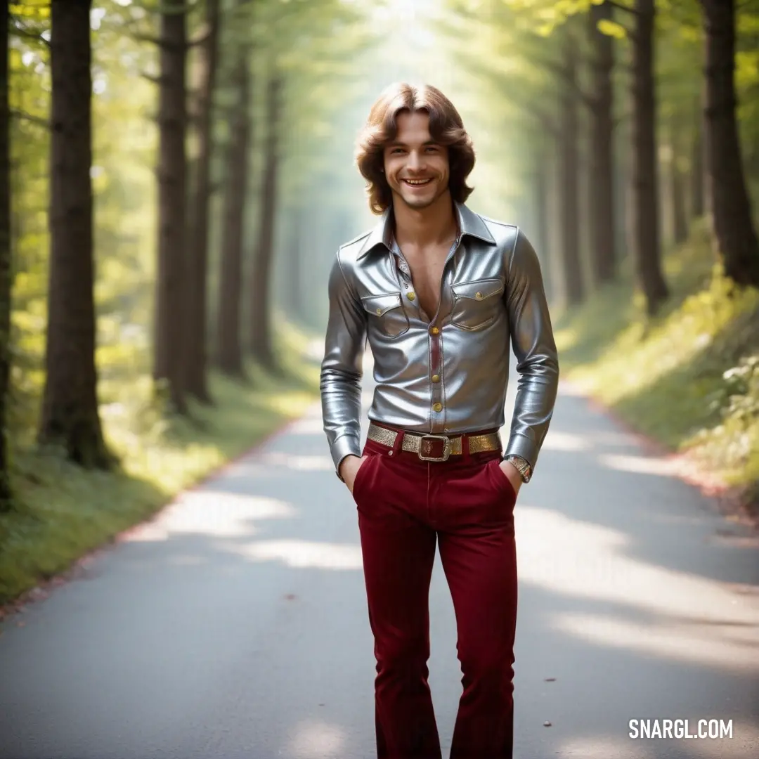 Man in a silver shirt and red pants standing on a road in the woods with trees in the background