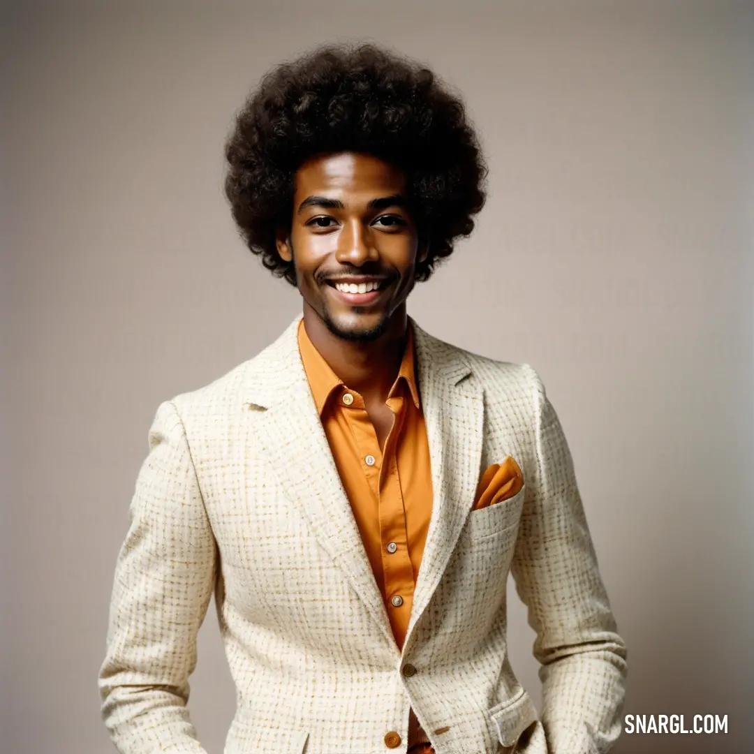 Man with an afro wearing a suit and orange shirt and tie and smiling at the camera with his hands in his pockets