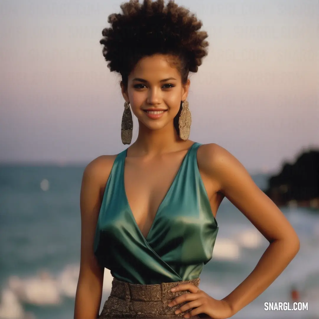 Woman with a green top and a pair of earrings on her head standing in front of the ocean