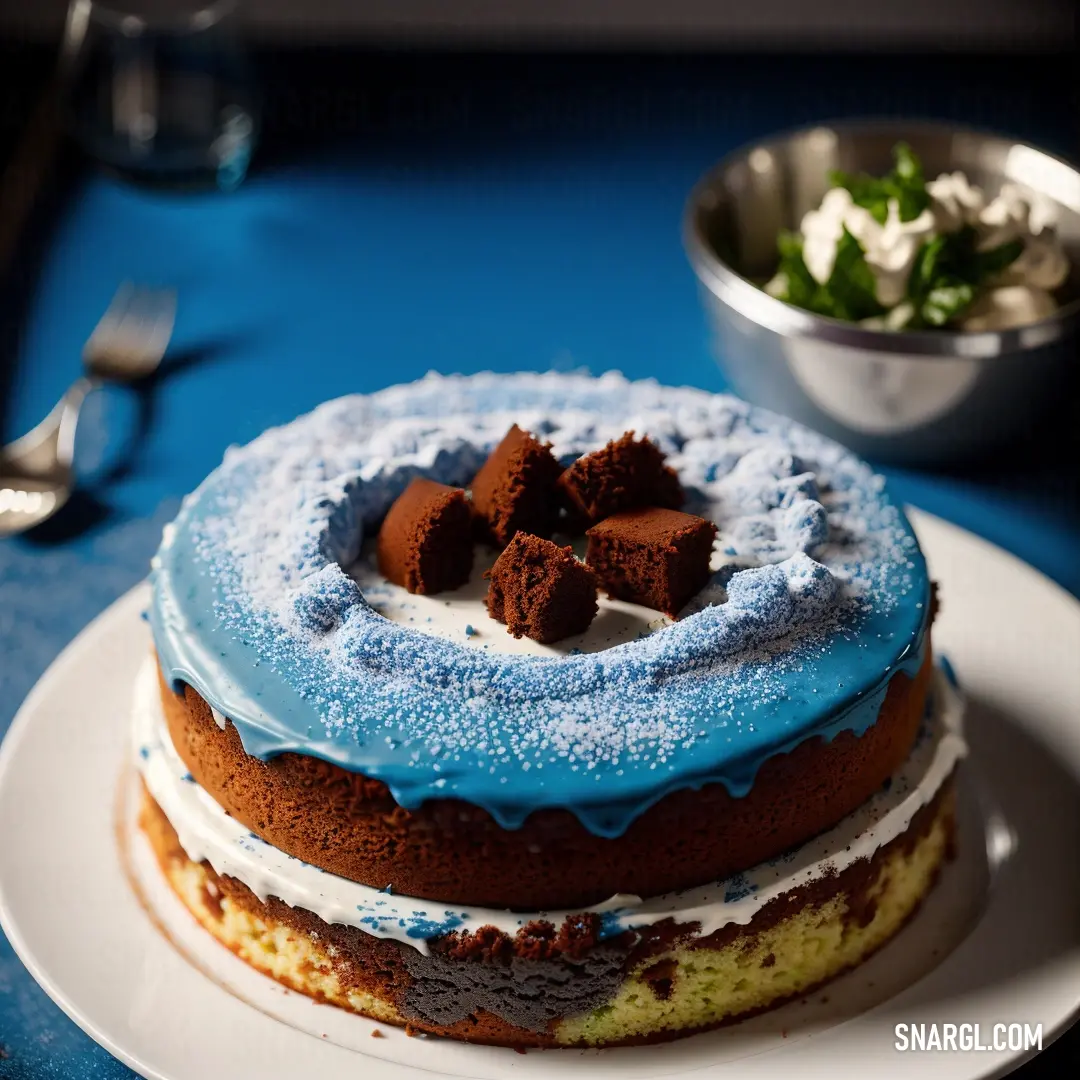 Cake with blue icing and chocolate pieces on top of it on a plate with a bowl of salad. Example of #5D8AA8 color.