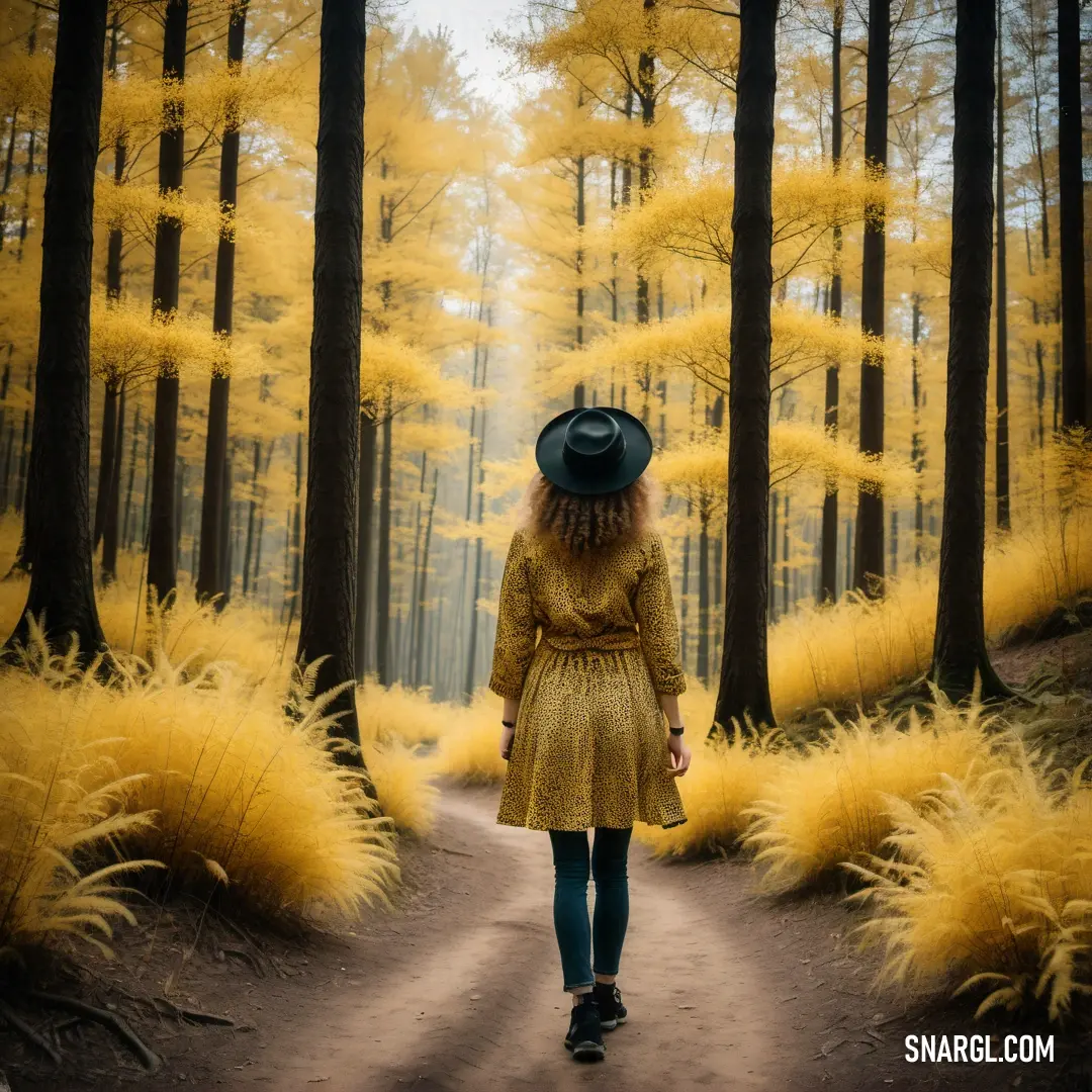Woman in a yellow dress and hat walking down a path in the woods with tall grass
