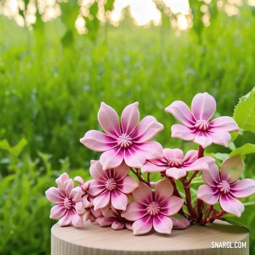 Small pink flower arrangement on a wooden table in a field of grass and trees in the background with a green leafy area