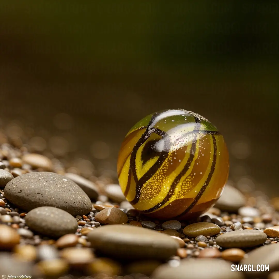 Yellow and black ball on top of a pile of rocks and gravel next to a green leaf