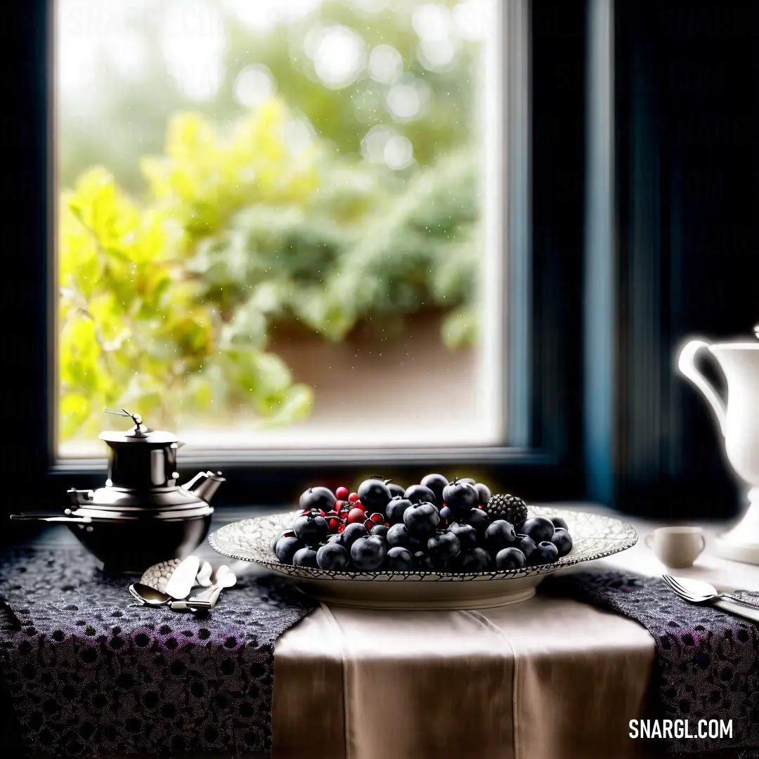 Plate of berries on a table near a window with a teapot and a cup on it