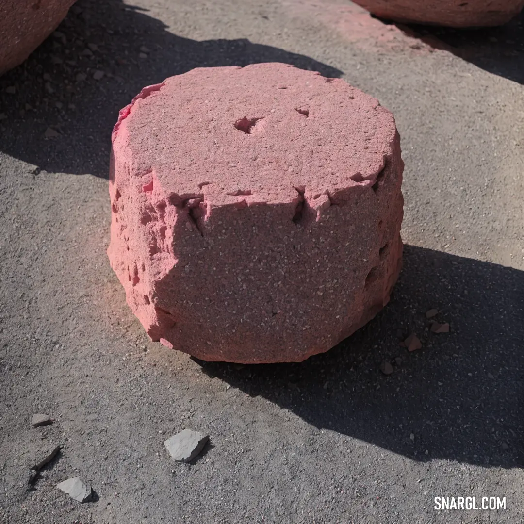 Red rock on top of a cement ground next to rocks and gravel balls on the ground and a person standing next to it