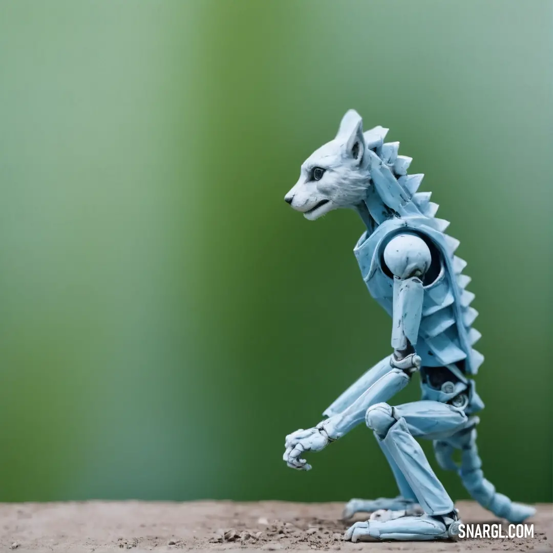 A small toy dog stands alert on a dirt path, with a lush green landscape in the background. The soft blue of the dog’s coat contrasts against the earthy tones of the dirt and the vivid green of the surrounding nature.