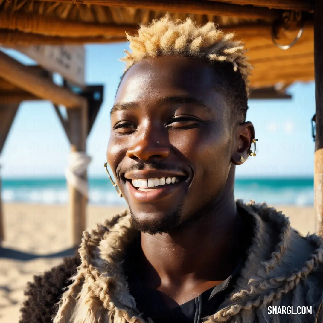 Man with blonde hair smiling at the camera on the beach with a blue sky in the background and a wooden structure in the foreground