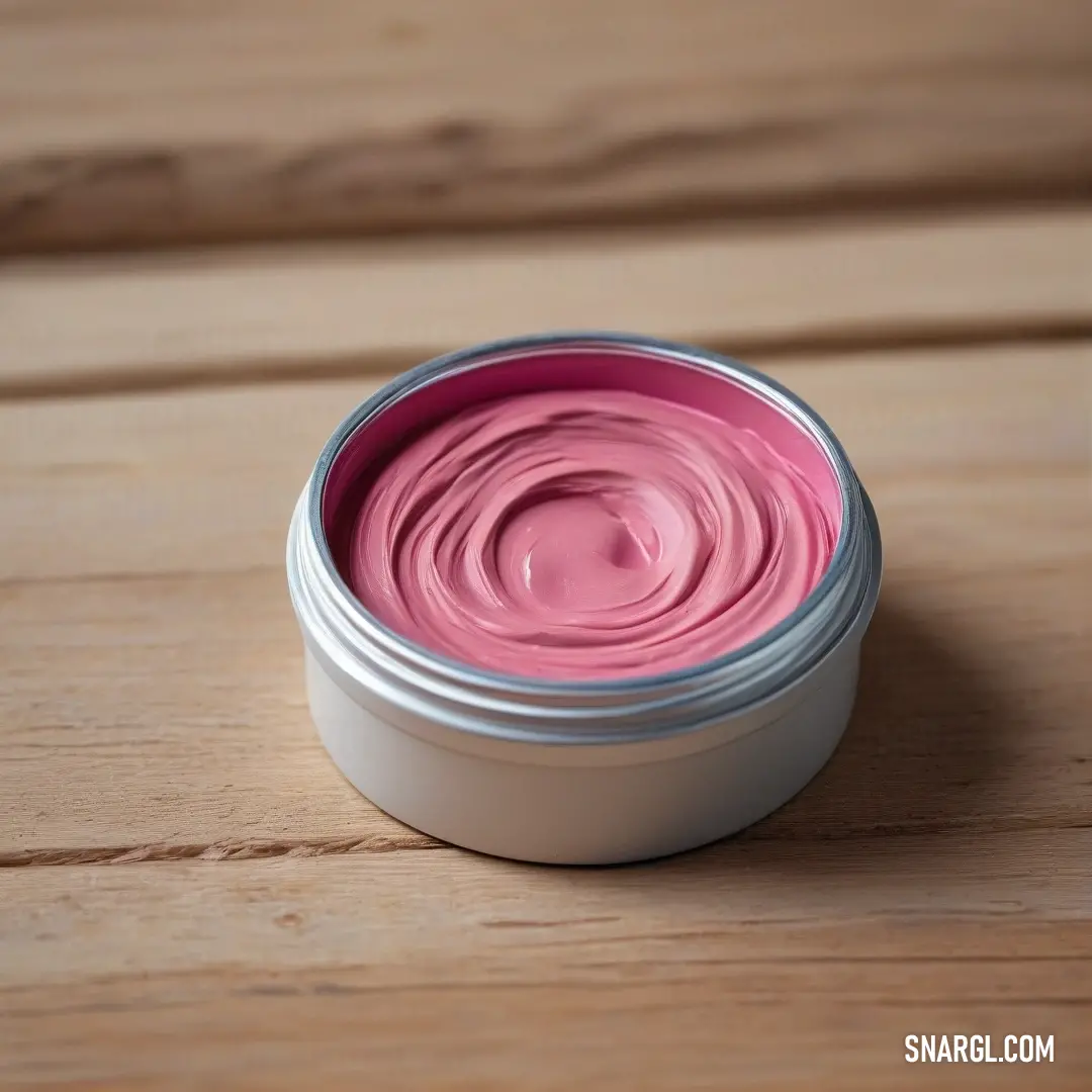 Pink lip polish in a small tin on a wooden table top. Example of Blush color.