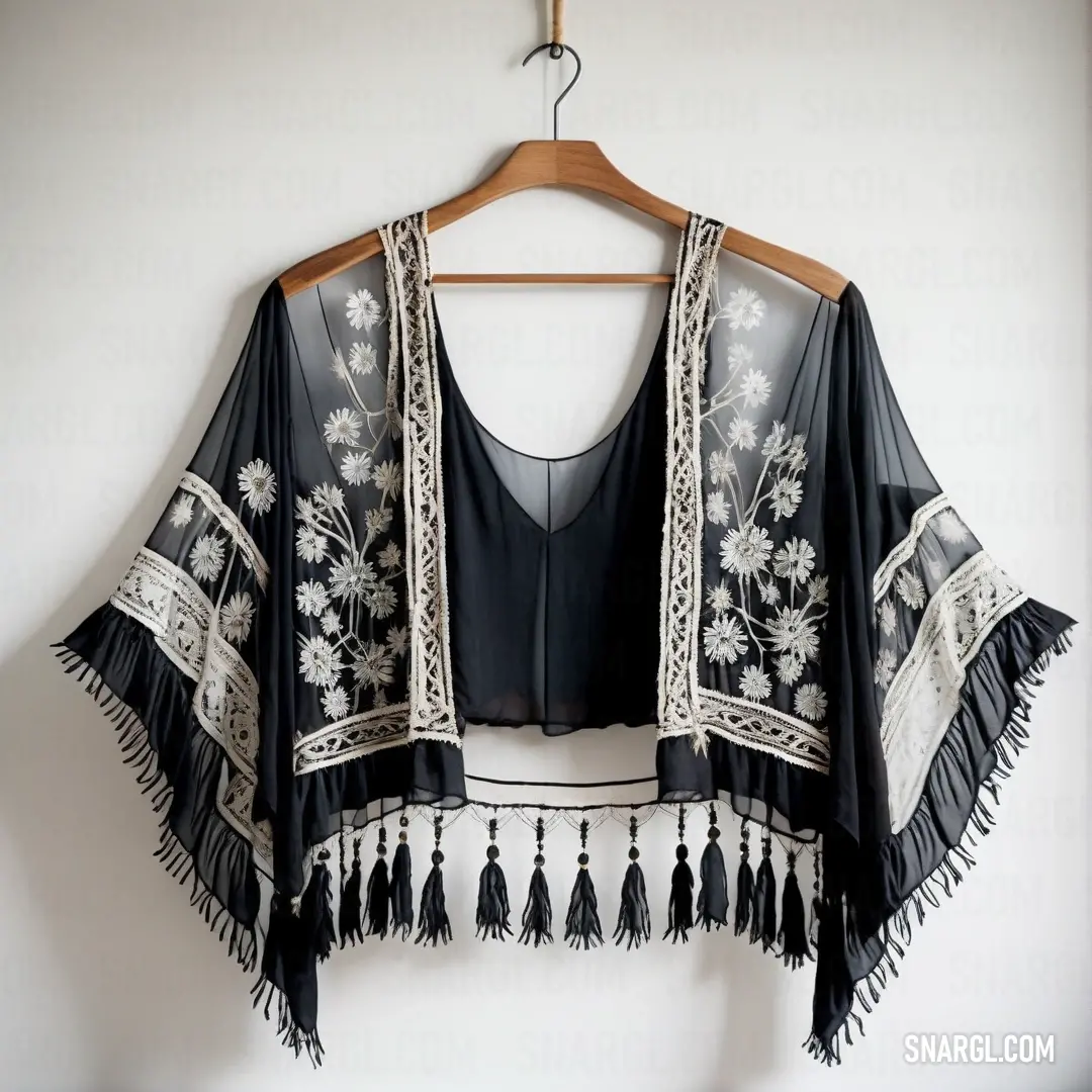 Black top with white flowers and tassels hanging on a hanger on a wall