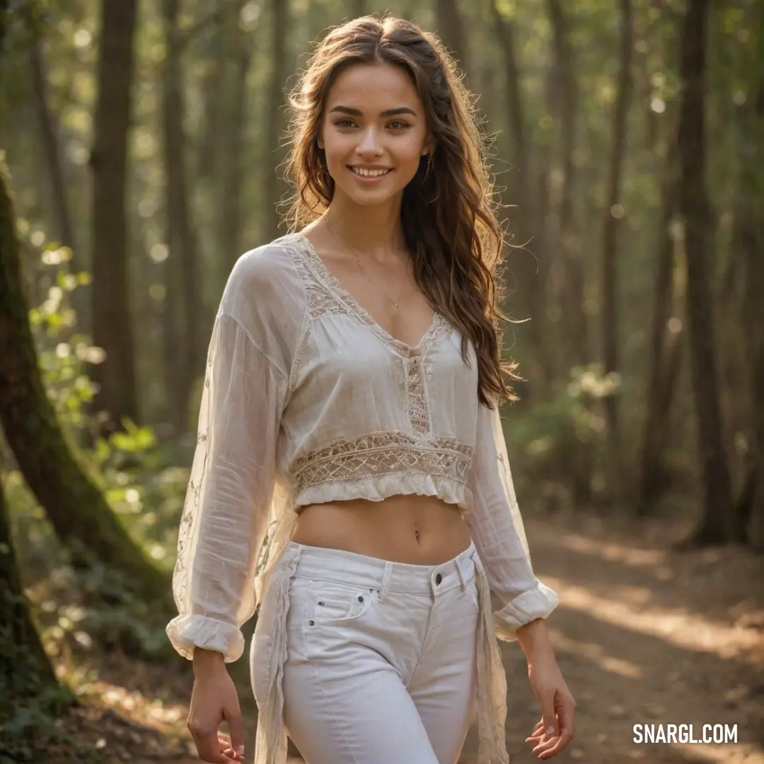 Woman in white pants and a white top walking through a forest with trees and a trail behind her