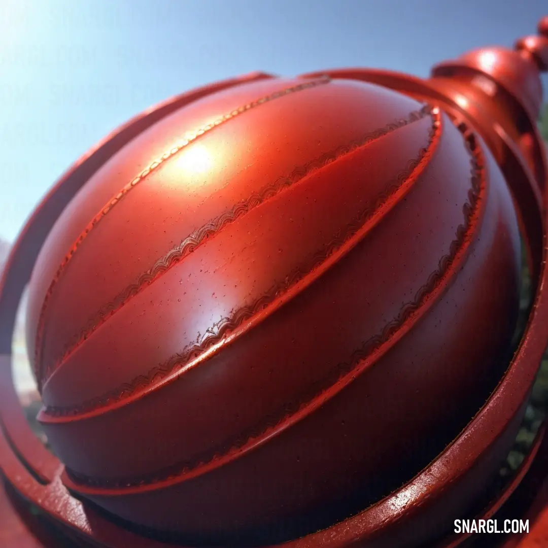 Red ball and a chain on a red pole with a blue sky in the background and a green bush