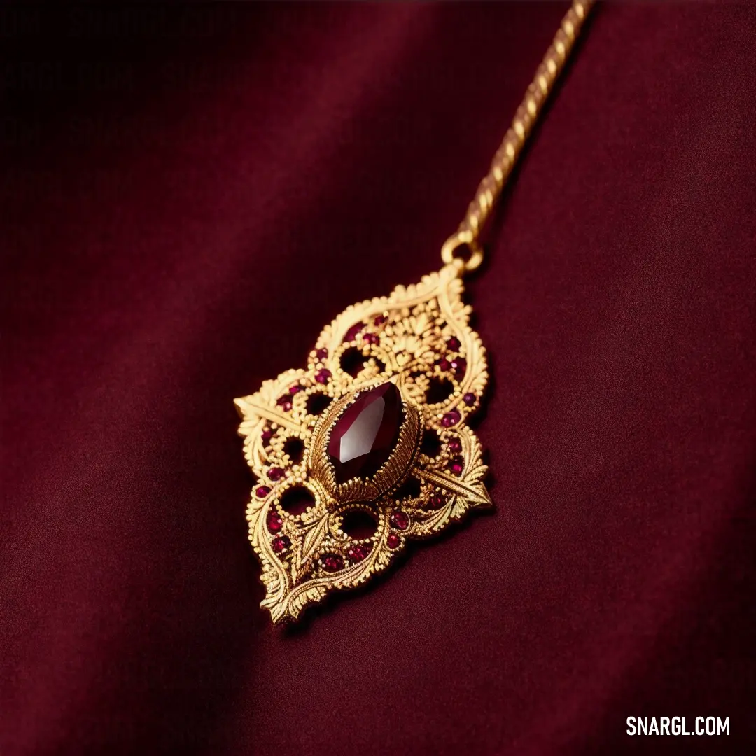 Gold necklace with a red stone on a red cloth background with a gold chain hanging from it's center