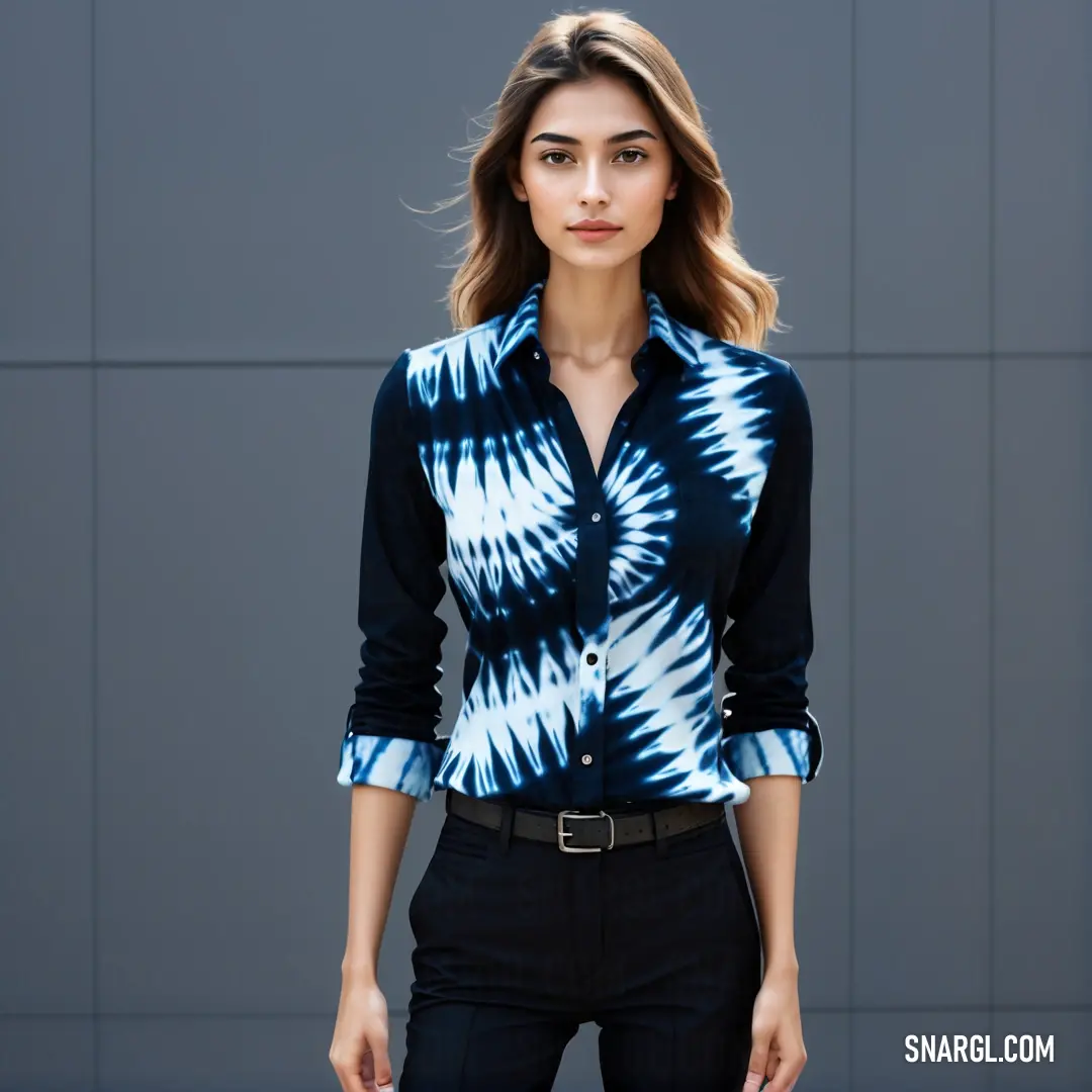 Woman in a tie - dyed shirt and black pants poses for a picture in front of a gray wall