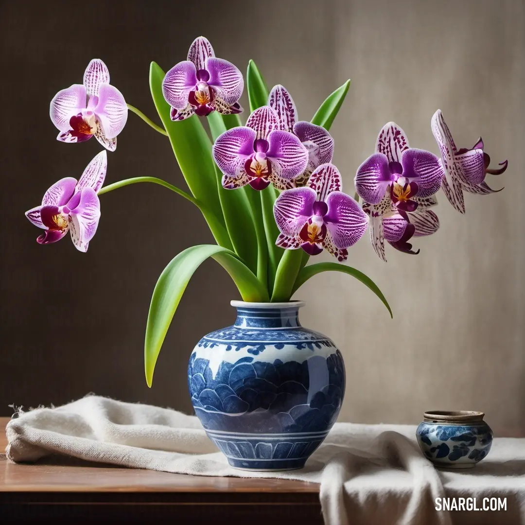 Blue vase with purple flowers in it on a table next to a white towel and a blue. Example of CMYK 0,63,12,56 color.