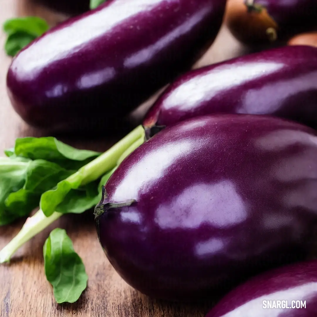 Close up of eggplant on a wooden surface with leaves and a knife in the background with a few other eggplant on the table