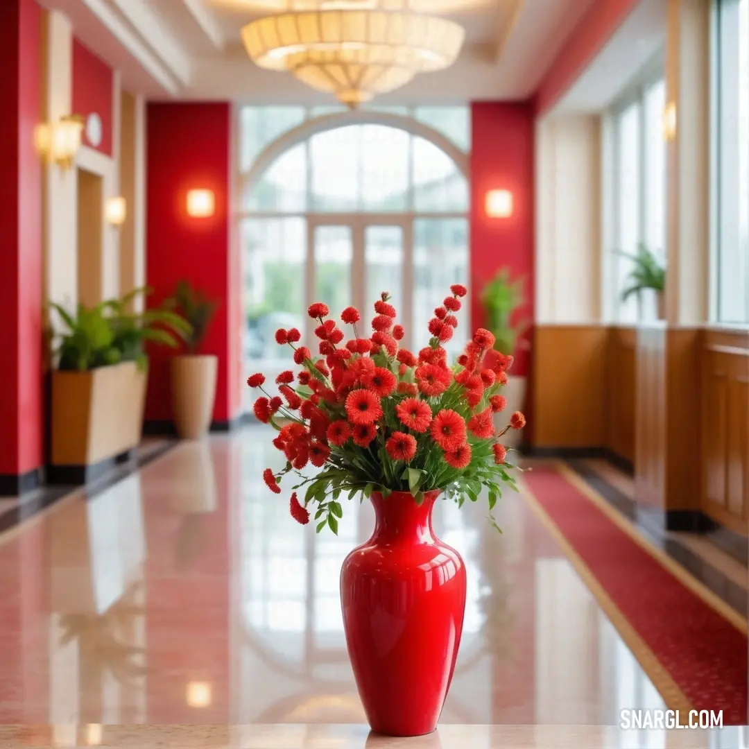 Red vase with red flowers in it on a table in a room with red walls and a chandelier. Color Cadmium red.