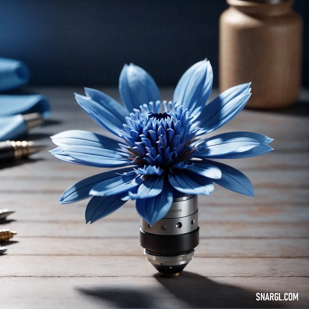 Blue flower on top of a wooden table next to a pen. Color Celestial blue.