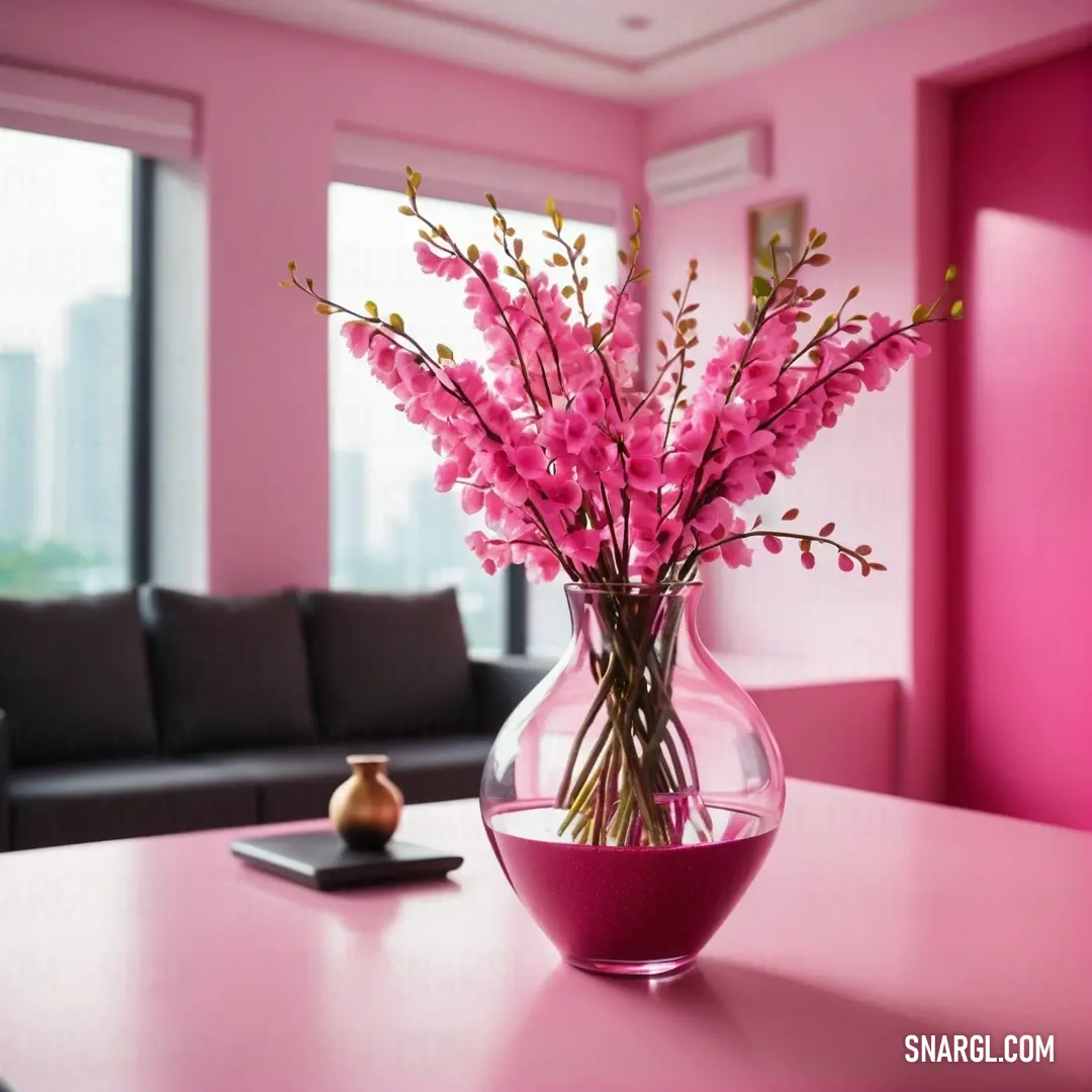 Vase with pink flowers in it on a table in a living room with a couch and window behind it. Example of #EC3B83 color.