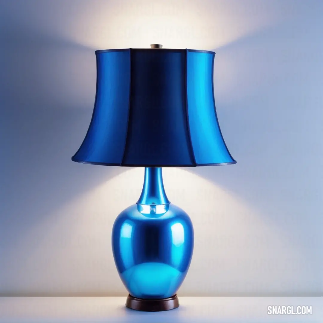 Blue lamp with a blue shade on a table top with a white wall behind it. Color Cobalt.