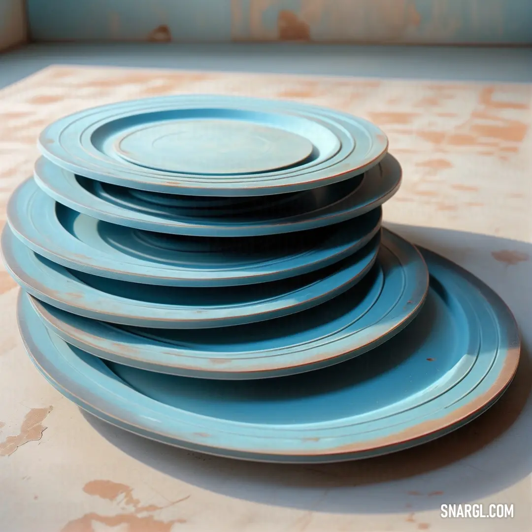Stack of blue plates on top of a table top next to a wall with a painting on it. Example of CMYK 39,13,0,0 color.
