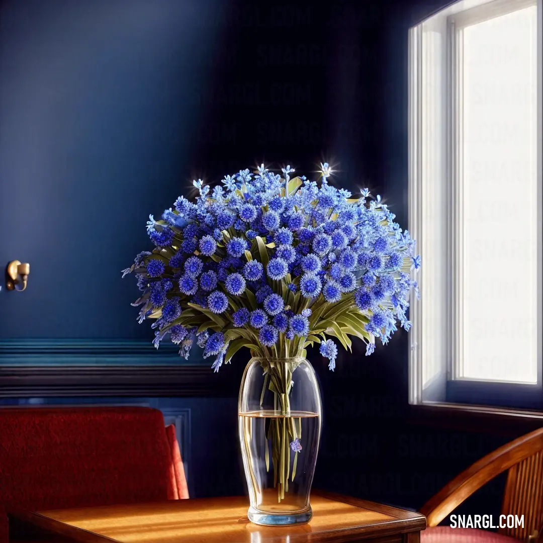 Vase of blue flowers on a table in a room with a chair and a window in the background