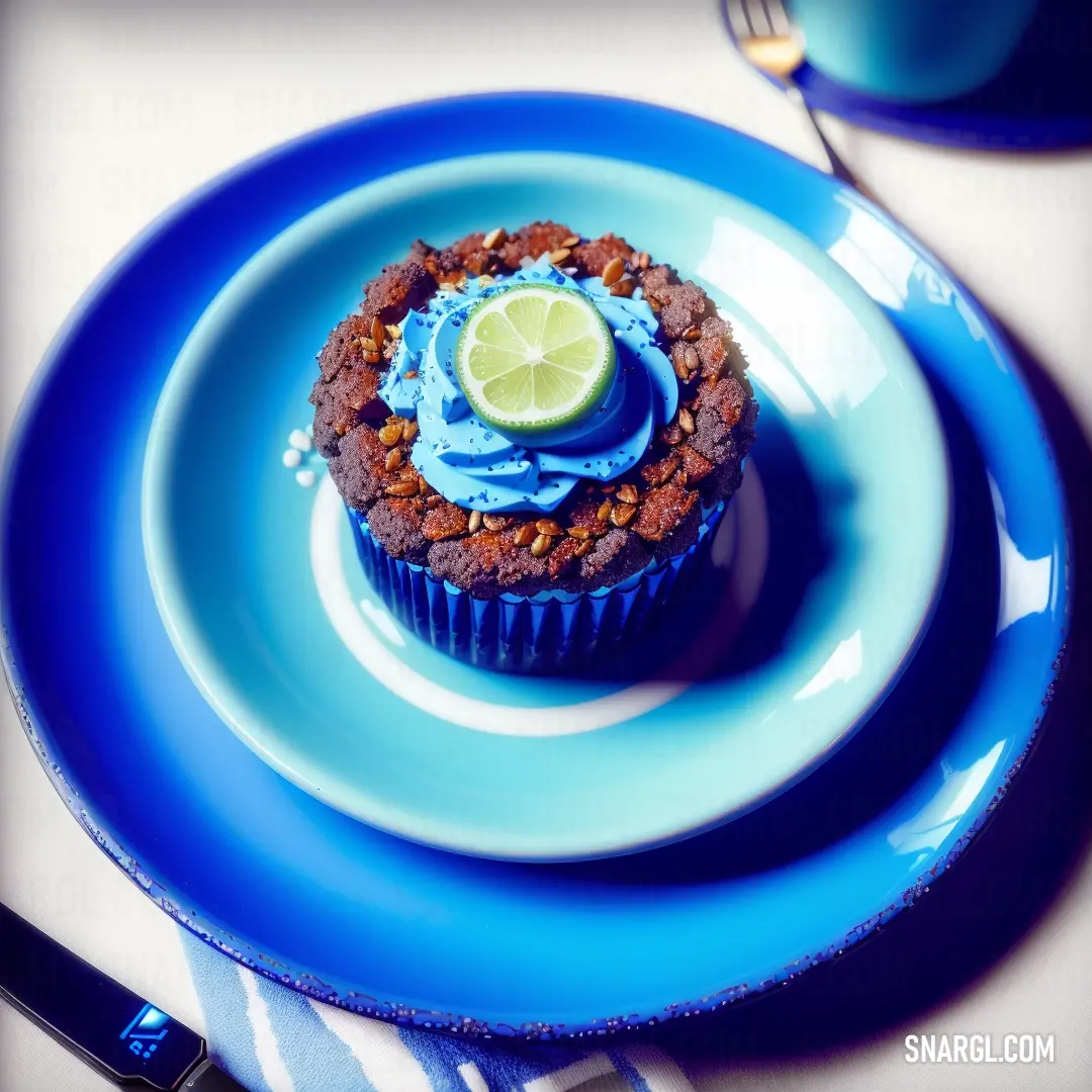 Cupcake with a lime slice on top of it on a blue plate with a fork and knife