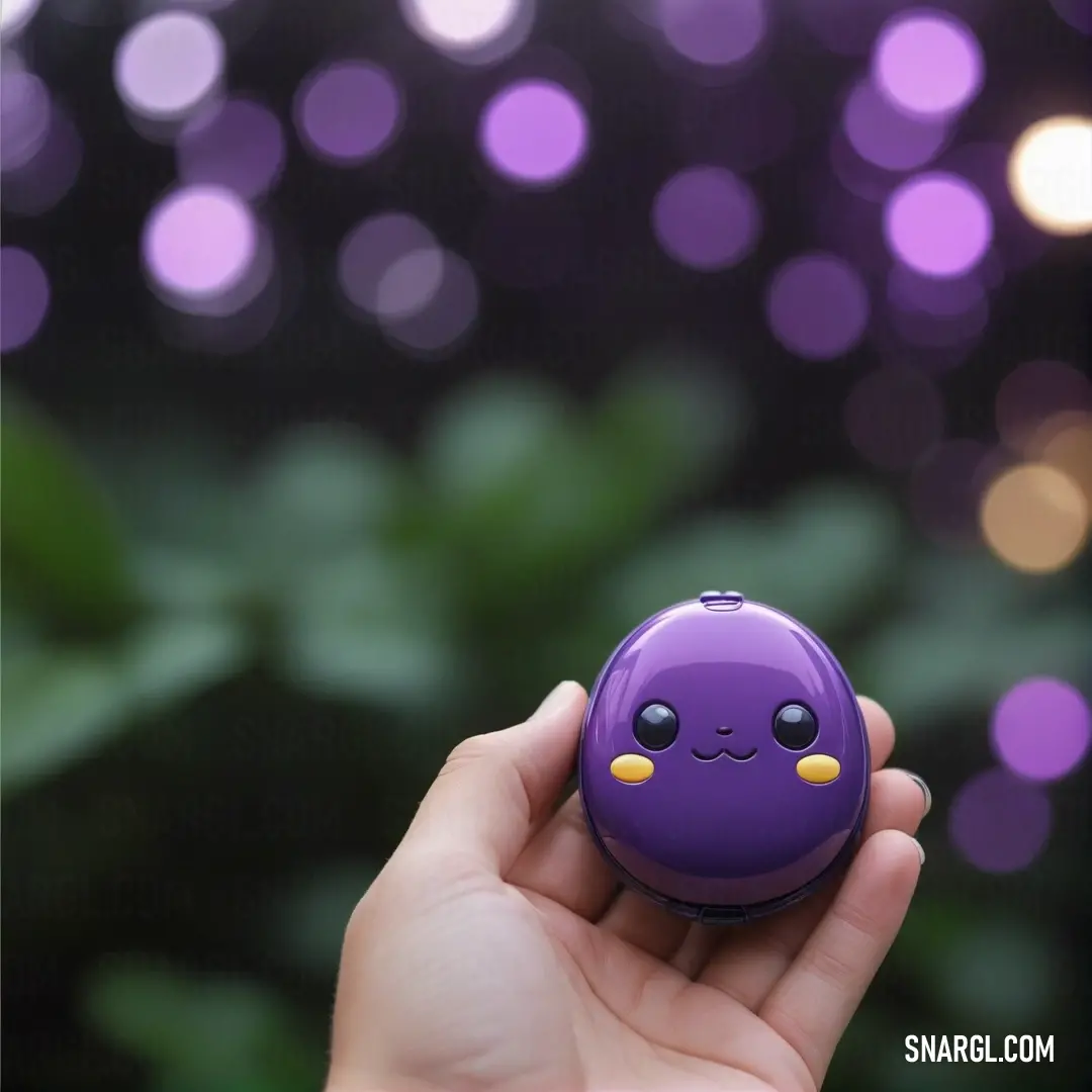 Hand holding a purple object with a smiley face on it's face. Color CMYK 23,47,0,41.