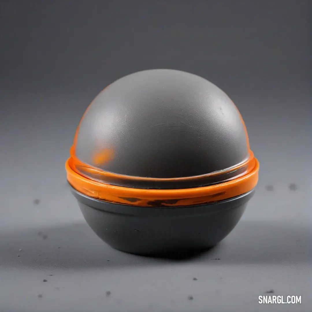 A gray and orange bowl with a lid sits on a table, set against a gray backdrop. The warm tones of the orange and the cool neutrality of the gray combine to create a balanced and harmonious scene.