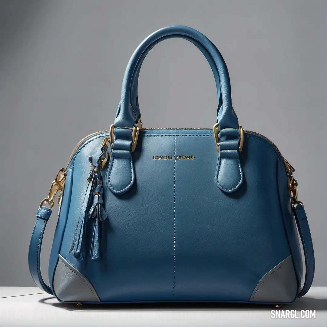 Blue purse with a tasseled handle and a tasseled strap on a table with a gray background. Color #779ECB.