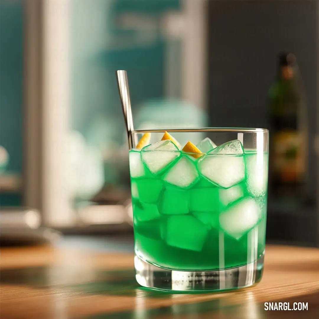 Green drink with ice and an orange slice in it on a table with a bottle of beer in the background