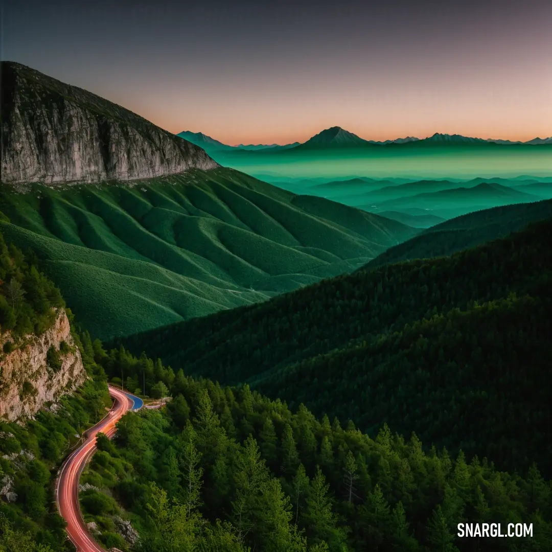 Winding road in the middle of a mountain range at sunset with a green glow on the mountains behind