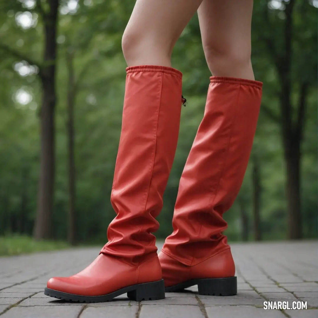 Woman wearing red boots standing on a brick walkway in front of trees and a forest in the background. Example of Dark pastel red color.