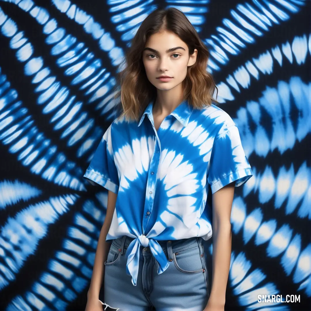 Dark powder blue color. Woman standing in front of a blue tie - dyed wall with her hands in her pockets and her shirt tied up