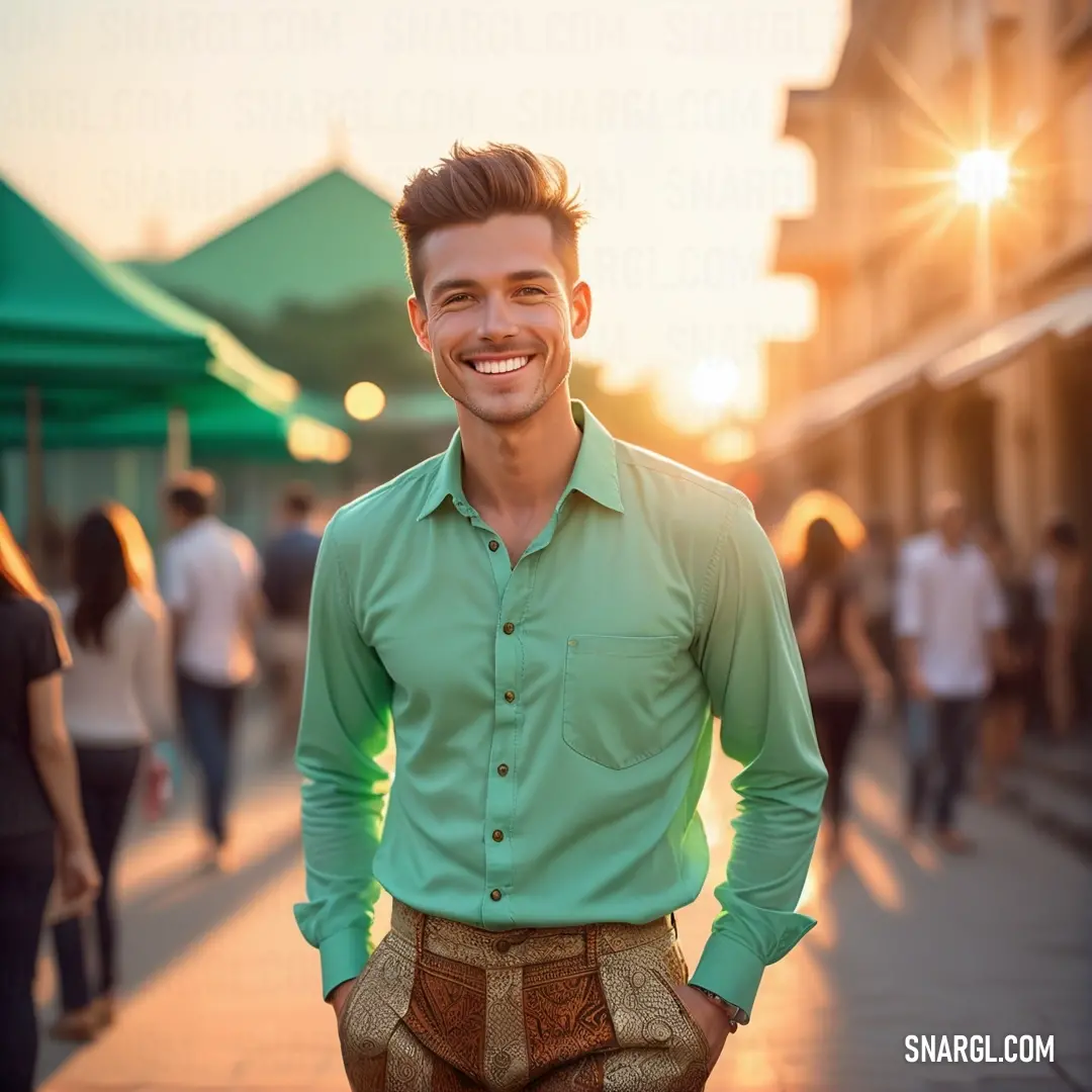 Man in a green shirt and brown pants standing on a sidewalk with his hands in his pockets and smiling. Color #8FBC8F.