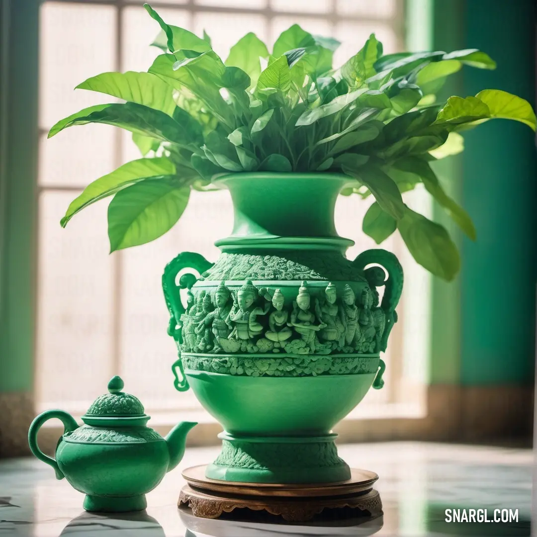 Green vase with a plant in it and a teapot on a table in front of a window. Color RGB 143,188,143.