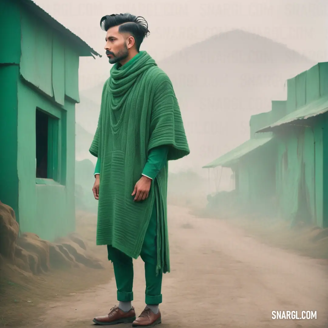 Man in a green shawl standing in a dirt road in front of a green building. Color Dartmouth green.