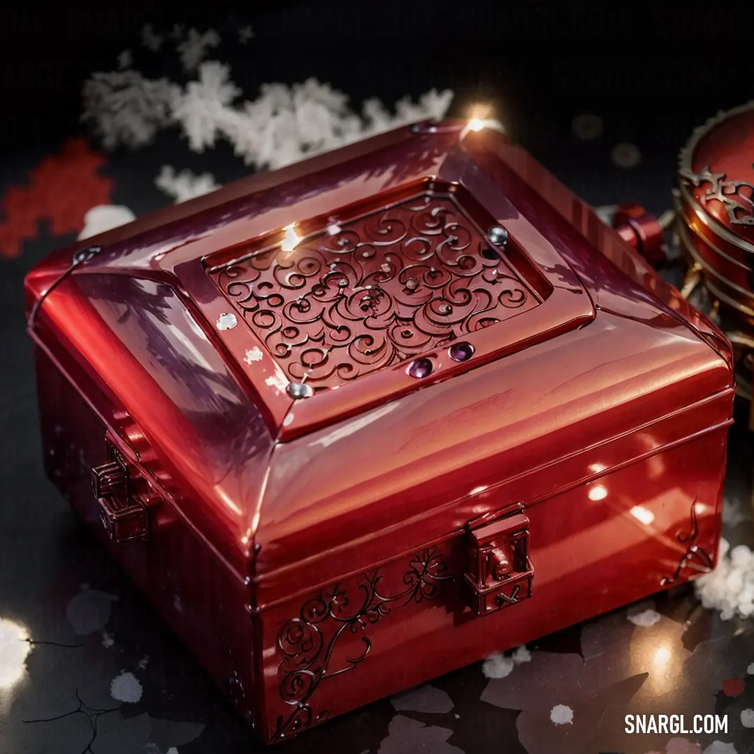 Red box with a decorative design on it and a candle on the side of it on a table