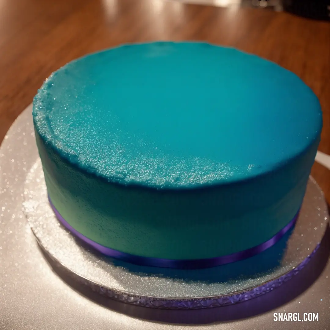 Blue cake on top of a white plate on a table with a purple ribbon around it and a blue frosting on top
