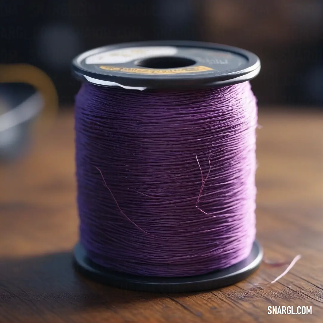 Spool of purple thread on a wooden table top. Example of CMYK 4,27,0,0 color.