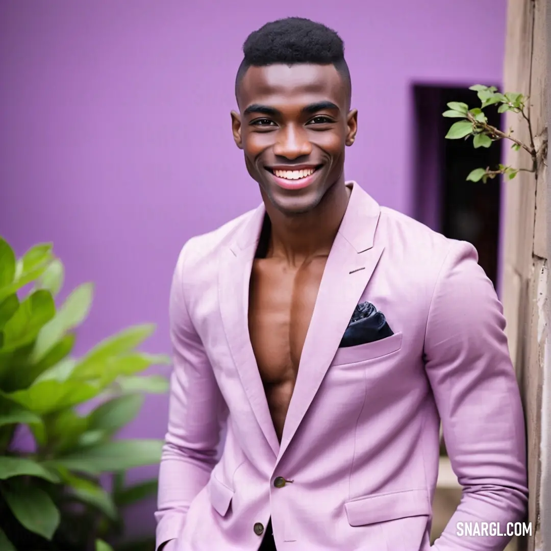 Man in a pink suit standing next to a purple wall and smiling at the camera with his shirt open. Color #F4BBFF.