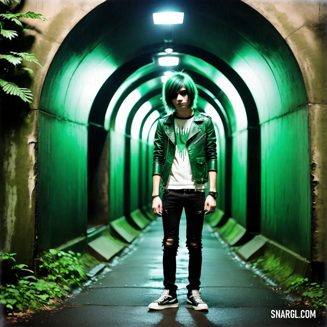 Man with green hair standing in a tunnel with green lights on either side of him and wearing a white shirt