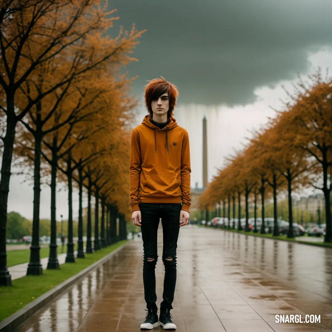 Man with red hair standing in the rain in a park with trees and a monument in the background