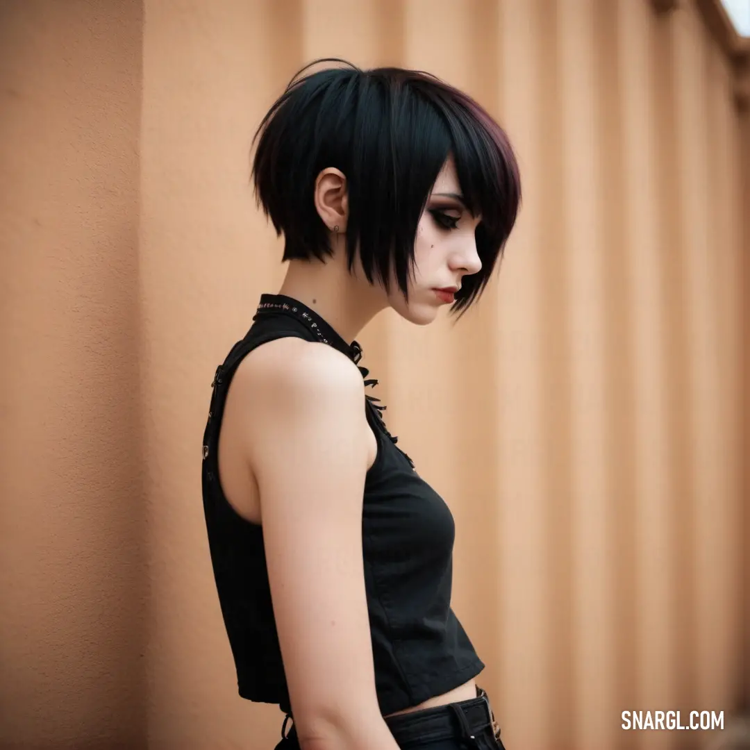 Woman with black hair and a black top is standing by a wall and looking off to the side