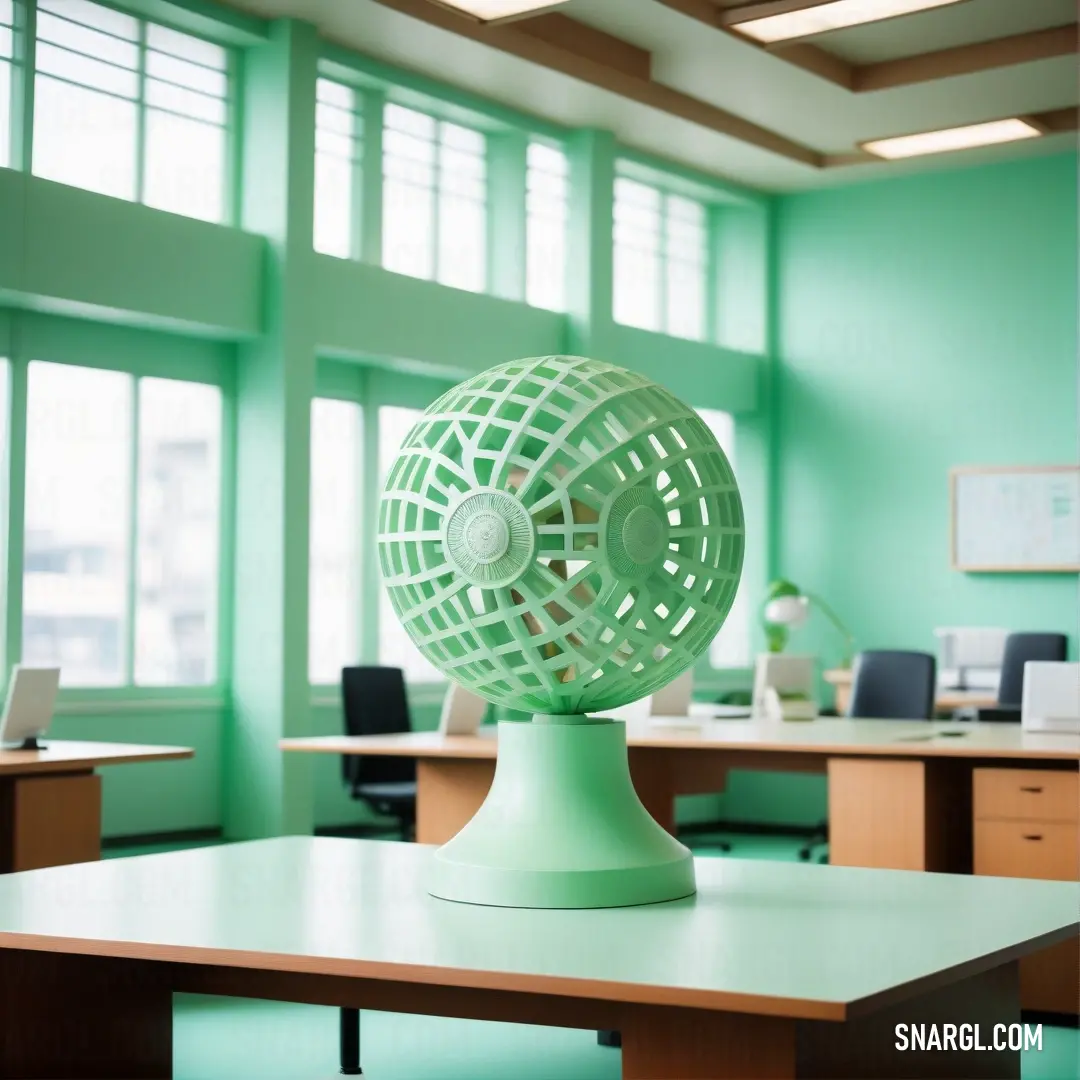 Green table with a green fan on top of it in a room with windows and a desk with a laptop. Color CMYK 25,0,19,22.