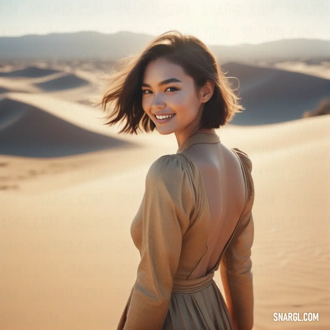 Woman standing in the sand dunes with her hair in the wind and smiling at the camera. Example of RGB 193,154,107 color.