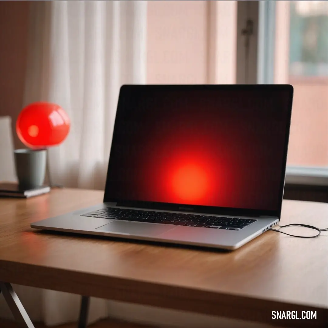 Laptop computer on top of a wooden desk next to a window with a red light on it. Color CMYK 0,84,100,0.