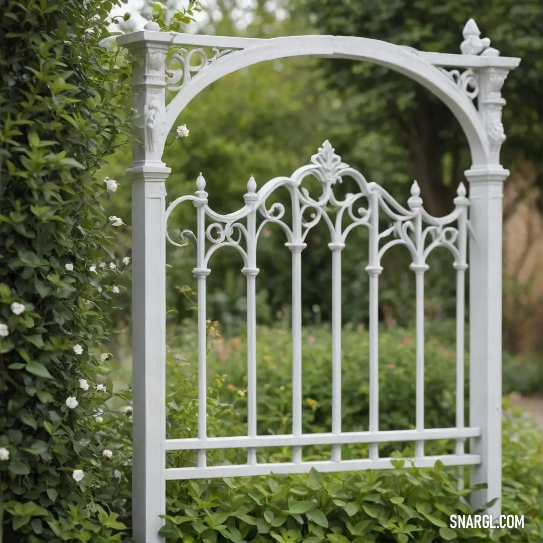 An inviting white iron gate opens gracefully into a lush garden, bordered by vibrant green hedges and shrubs. A winding path leads the way, promising delightful discoveries in this serene sanctuary awash in the gentle hues of CMYK 0,26,45,35.